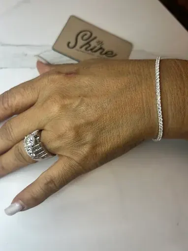 Wrist wearing a delicate tennis bracelet and a wide silver ring with a center stone, Shine card in the background