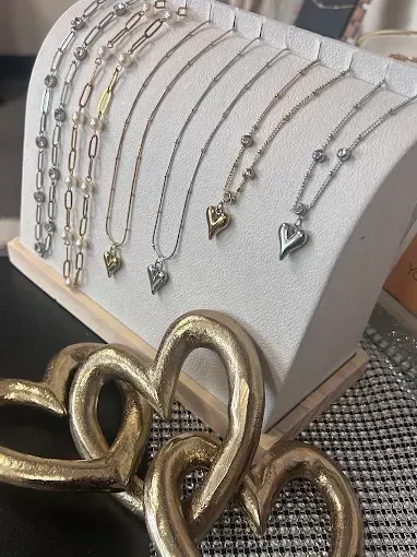 Six dainty gold and silver necklaces with hearts, pearls, and stones displayed on a white jewelry stand