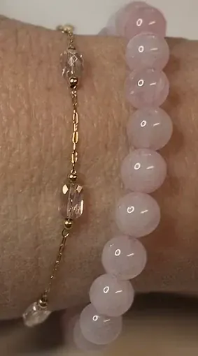 Wrist wearing a gold chain with clear faceted beads stacked with a pale pink bead bracelet