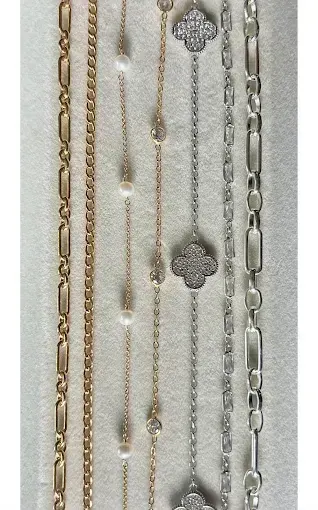 Seven gold and silver chain styles laid side by side on a light jewelry tray, from figaro to paperclip