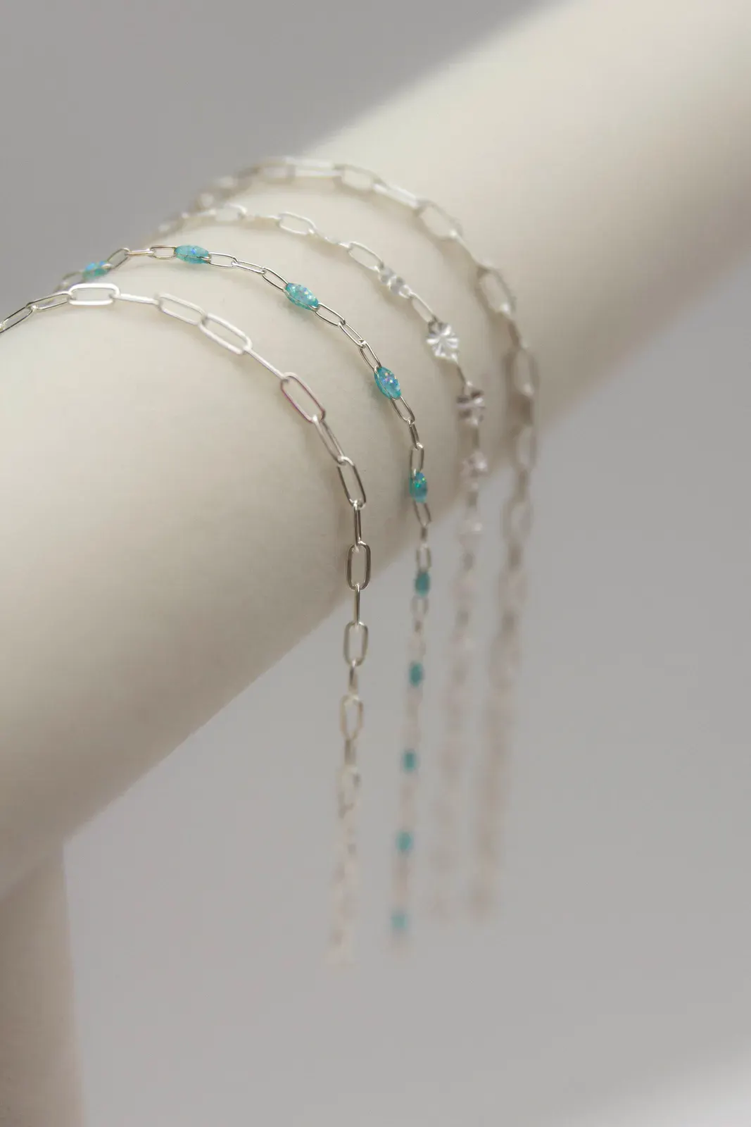 Three silver bracelets stacked on a wrist: a tennis bracelet, a mixed-stone station bracelet, and an infinity curb