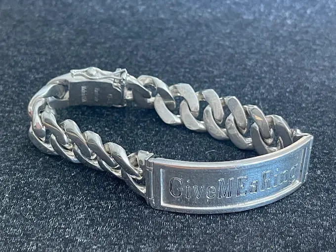 Polished silver Cuban-link ID bracelet with a central nameplate on a dark textured surface