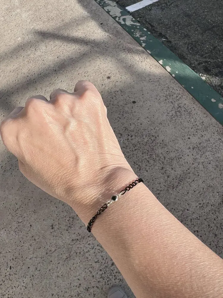 Black chain bracelet with a round black gemstone in a silver bezel on a wrist outdoors