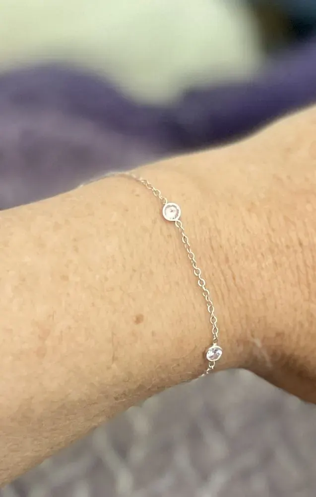 Close-up of a thin silver cable bracelet with two small bezel-set clear stones on a wrist