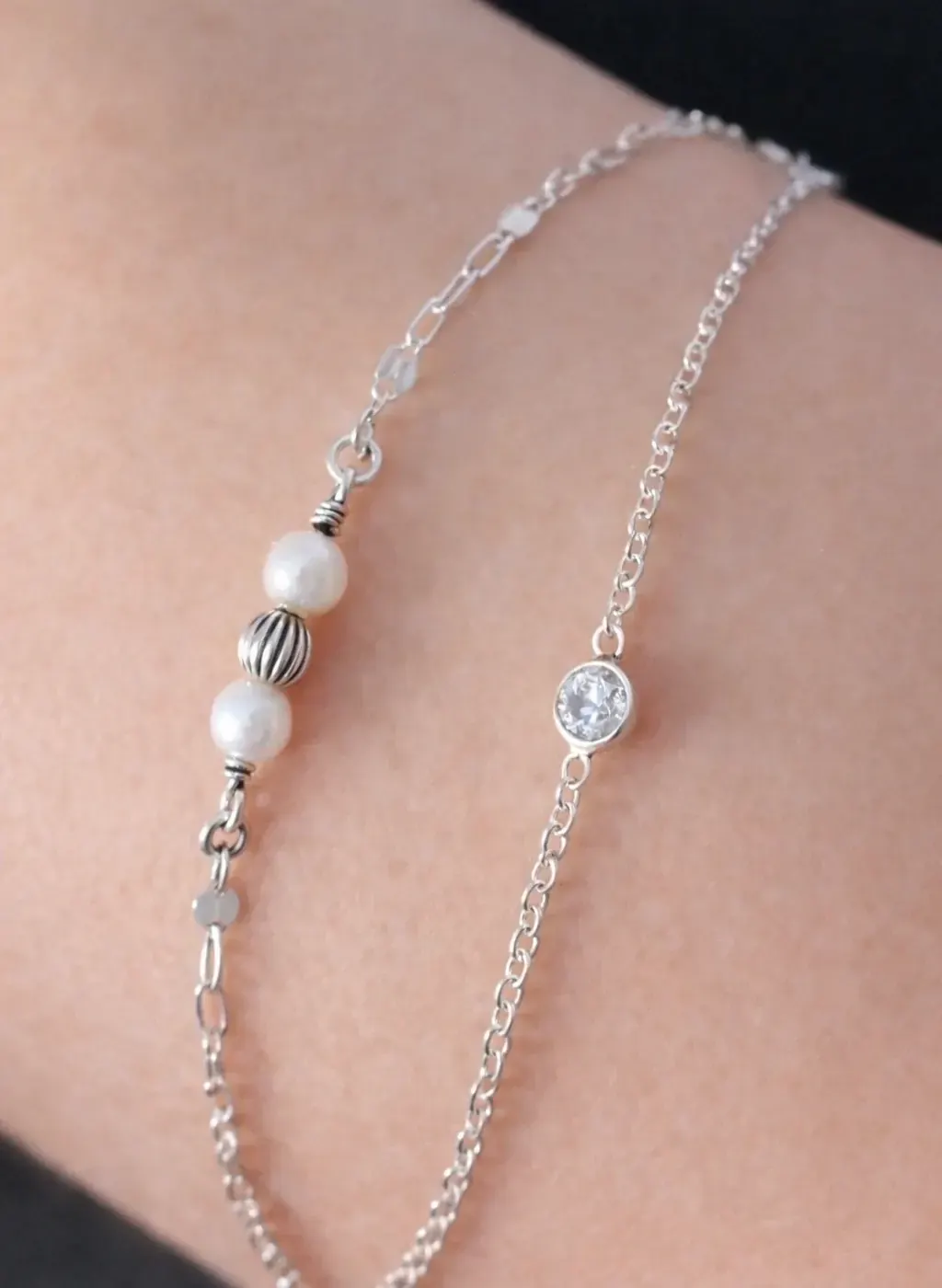 Close-up of a double-strand silver bracelet with two white pearls, a textured silver bead, and a small bezel-set stone