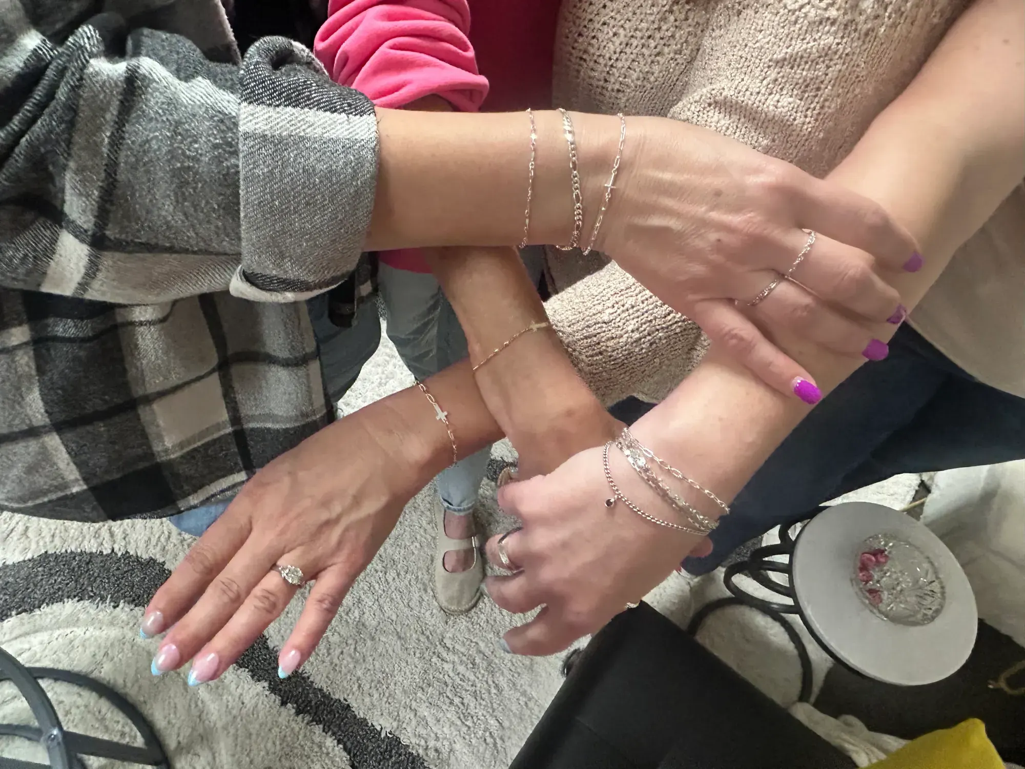 Four friends stack their wrists in a circle, each wearing a chain bracelet.